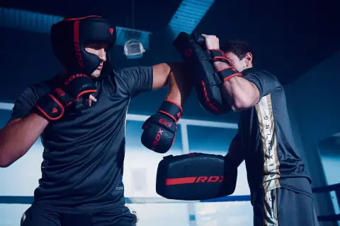 Two boxers in a ring, one wearing a headguard and gloves, practicing sparring with pads.