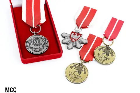 Odznaczenia strażackie w pudełku i luźno leżące na białym tle. Widać godło Polski i symbole strażackie.