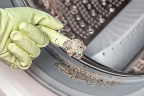 Mit einem Gummihandschuh wird Schmutz aus der Waschmaschine entfernt.