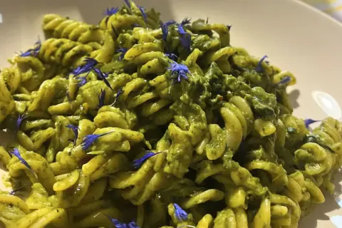 Fusilli-Pasta mit einer cremigen grünen Soße, garniert mit blauen Kornblumen. Ein köstliches italienisches Palmkohl Rezept.