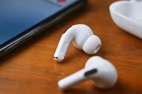 Białe słuchawki JBL leżą obok iPhone'a i etui. Dowiedz się, jak podłączyć słuchawki JBL do iPhone'a, by cieszyć się muzyką.