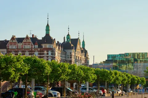 Kopenhaga ceny: zabytkowe budynki i nowoczesna architektura nad wodą, z rzędem drzew i zaparkowanymi samochodami.