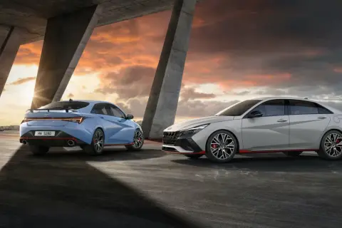Dwa sportowe Hyundai sedan w kolorach niebieskim i jasnoszarym stoją pod betonowym mostem podczas zachodu słońca.