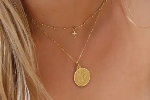 Elegante cadena de oro con medalla de San Benito y un pequeño crucifijo.