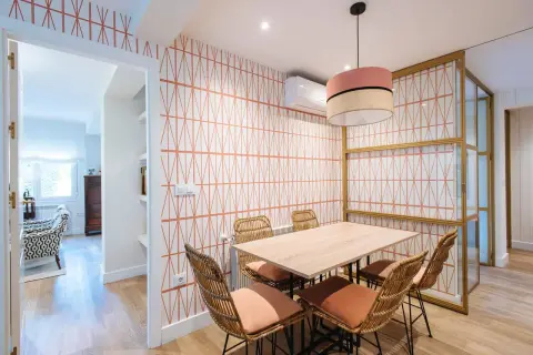 Comedor con papel pintado de rombos naranjas, mesa de madera y sillas de mimbre. Un ejemplo de como poner papel pintado para renovar tu hogar.
