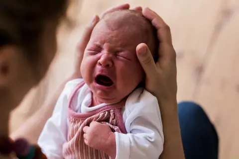 Ein Neugeborenes schreit laut, während es von Eltern gehalten wird. Die Frage, warum schreien Babys nach der Geburt, beschäftigt viele.