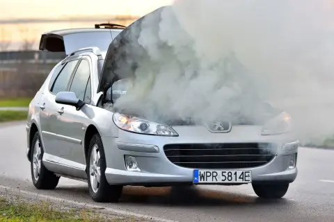 Srebrny Peugeot z otwartą maską i kłębami dymu. Chyba ten rozbiegany diesel potrzebuje pomocy.