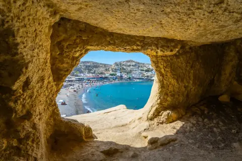 Blick durch eine Höhle auf einen belebten Strand und das türkisfarbene Meer. Ein perfekter Ausschnitt der Kreta Highlights.
