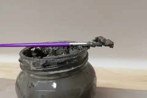 Pinceau violet trempé dans une pâte grise, prête à recoller terre cuite.