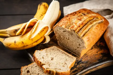 Pyszne, wilgotne ciasto bananowe, które zawsze się udaje. Obok leżą dojrzałe banany, gotowe do pieczenia.