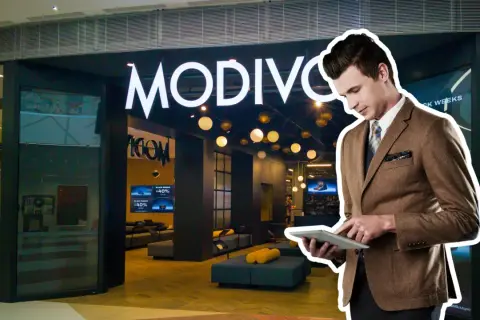 Elegancki mężczyzna w garniturze przegląda tablet przed sklepem MODIVO. W tle widać promocje CCC GPW.