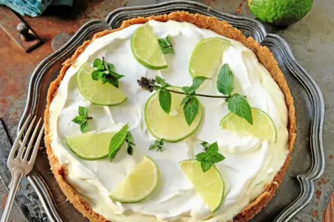 En krämig key lime pie med limeklyftor och mynta på en krispig botten.