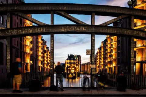 Spektakuläre Fotografie Hamburg: Speicherstadt im Abendlicht, beleuchtete Backsteingebäude spiegeln sich im Wasser.