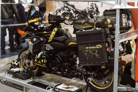 Czarny motocykl BMW R1250 GS z żółtymi akcentami, przygotowany do transportu motocykla w busie. Na kufrach mapy świata i naklejki.