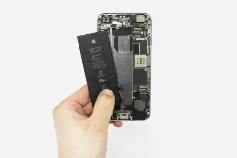 Dłoń wyjmuje baterię z otwartego iPhone'a 6s.