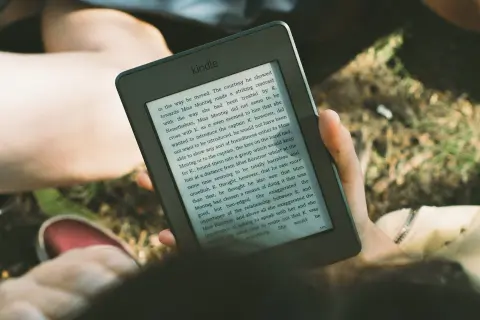 Une personne lit un livre sur une liseuse, profitant du soleil. L'encre numérique offre une lecture confortable en extérieur.