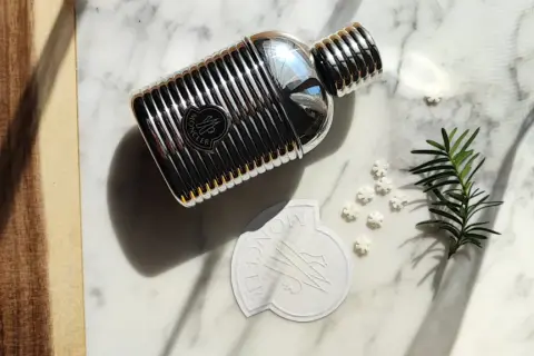 Elegancki flakon perfum Moncler pour homme na marmurowym tle, otoczony gałązką iglaków i płatkami śniegu.