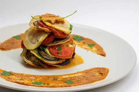 Ein gestapeltes Ratatouille-Rezept auf einem Teller, garniert mit Sauce und Kräutern.