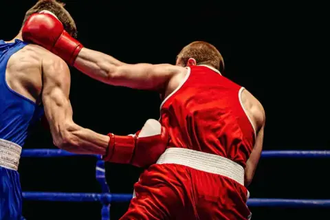 Boxers in a ring. The boxer in red throws a punch, showing how to know if your southpaw or orthodox by their stance.