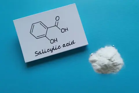 Kwas salicylowy na twarz: biały proszek i jego wzór chemiczny na kartce.