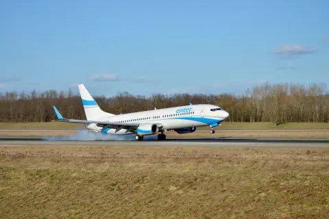 Samolot Enter Air ląduje, koła dotykają pasa, unosząc pył.