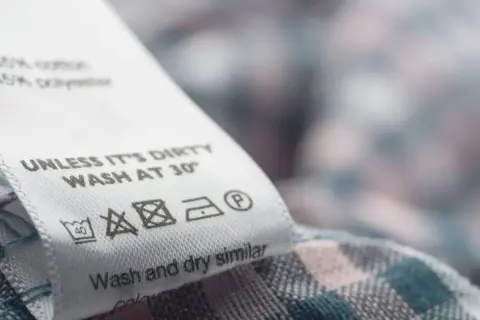 Metka z instrukcją prania: prać w 30°C, nie wybielać, prasować w niskiej temperaturze, czyścić chemicznie. Nazwy materiałów: bawełna, poliester.