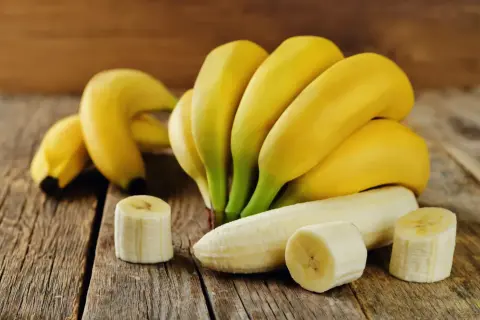 Kilka dojrzałych bananów, jeden obrany i pokrojony, na drewnianym blacie. Zastanawiasz się, ile cukru ma banan?
