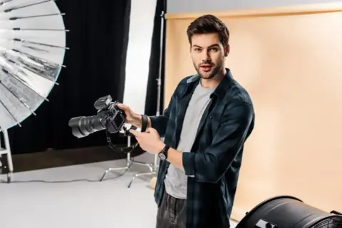 Młody fotograf z aparatem w studio. Świetna robota!