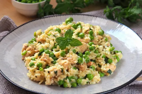 Pyszne risotto z groszkiem i kawałkami kurczaka, udekorowane listkiem mięty. Idealne na lekki obiad.