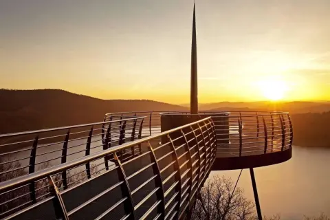 Ein Skywalk NRW bei Sonnenuntergang mit Blick auf einen See und bewaldete Hügel.
