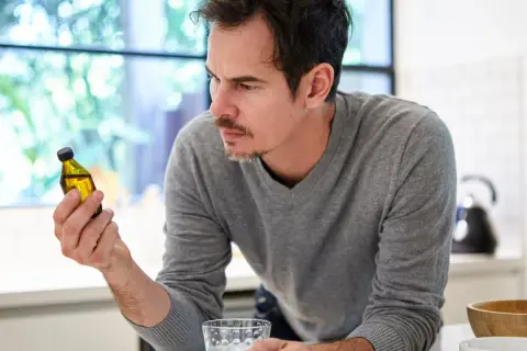 Uomo pensieroso guarda una fiala di liquido giallo, chiedendosi se la vitamina B12 fa ingrassare.