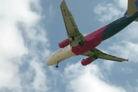 Samolot Wizz Air z wysuniętym podwoziem na tle nieba z chmurami.