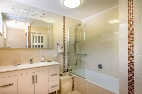 Baño moderno con ducha y bañera, lavabo con mueble y espejo decorado con un lagarto. El alicatar baño resalta con detalles en mosaico.