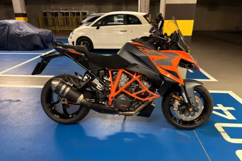 Pomarańczowo-szary KTM 1290 Super Duke w garażu, obok białego Fiata 500.