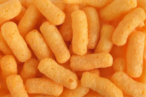 Zbliżenie na stos chrupek kukurydzianych w kolorze pomarańczowym.