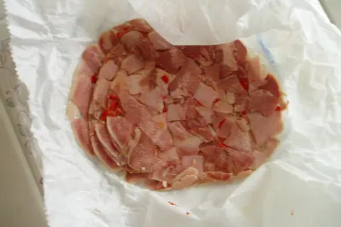 Rebanadas de queso de cabeza con trozos de pimiento rojo, envueltas en papel blanco.