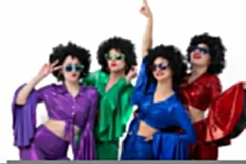 Kolorowa stylizacja na andrzejki: cztery kobiety w perukach afro i błyszczących strojach disco, z okularami przeciwsłonecznymi, tańczą i pozują.