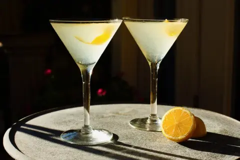 Dwa drinki z wódką waniliową i cytryną, podane w kieliszkach martini na kamiennym stoliku.