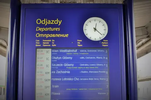 Tablica odjazdów PKP z zegarem. Widoczne pociągi do Wiednia, Olsztyna, Szczecina, Warszawy Zachodniej i innych. Kiedy zmiana rozkładu jazdy PKP, warto sprawdzić tablicę.