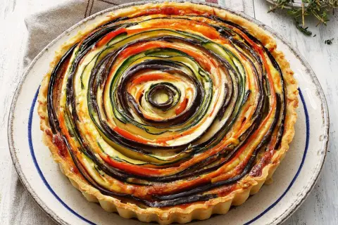Quiche de verduras con hojaldre, un remolino de calabacín, berenjena y tomate sobre una base dorada.