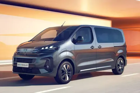 Nowy Peugeot e-Traveller, czyli ile waży bus 9-osobowy, pędzi po drodze na tle pomarańczowych ścian.