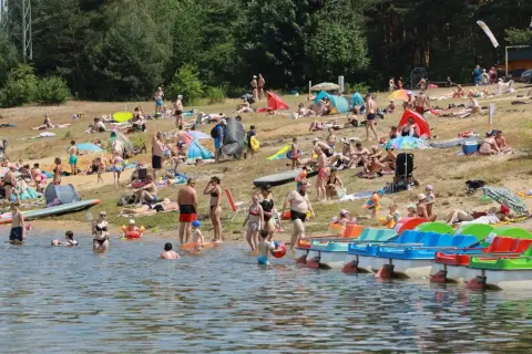 Tłum ludzi wypoczywa na plaży nad jeziorem Nakło Chechło. Woda jest spokojna, a na brzegu widać kolorowe rowerki wodne.