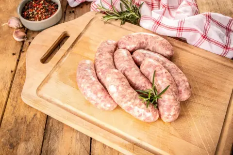 Surowa biała kiełbasa na desce, gotowa do przygotowania. Zioła i przyprawy dodają apetycznego wyglądu.