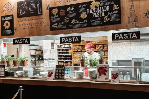 W Vapiano kucharz przygotowuje ręcznie robiony makaron. Na ścianie menu z różnymi rodzajami pasty.