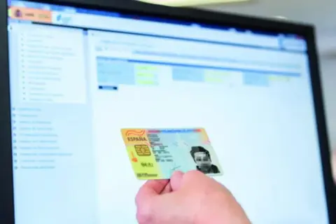 Mano sostiene DNI español frente a pantalla de ordenador con interfaz de gestión. Apoderamiento DGT.
