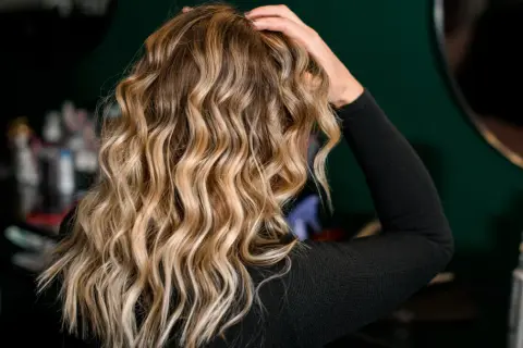 Blond włosy z pięknymi falami, podkreślonymi przez aktywator skrętu włosów. W tle widać kosmetyki fryzjerskie.