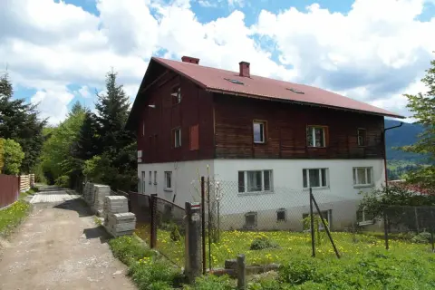 Stacja turystyczna Abrahamów, drewniano-betonowy budynek z czerwoną dachem, otoczony zielenią i polnymi kwiatami.