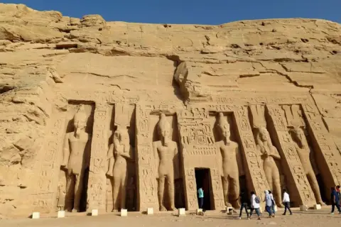 Gigantescas estatuas talladas en la roca flanquean la entrada del templo de Abu Simbel. Turistas admiran la majestuosidad de este sitio histórico.