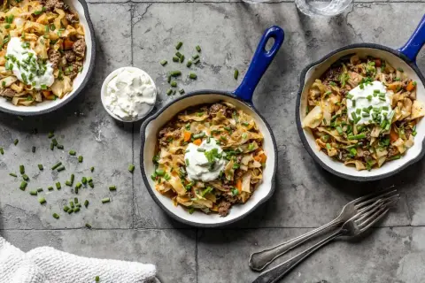 Herzhafte spitzkohl rezepte mit hackfleisch, garniert mit einem Klecks Sauerrahm und Schnittlauch, serviert in kleinen Pfannen.