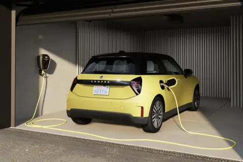 Żółty elektryczny Cooper w garażu, podłączony do ładowarki. Idealny wybór dla leasingu konsumenckiego samochodu.